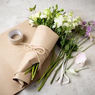 Kraft paper flower wrapping, paper tape and natural twine arranged beside fresh stems